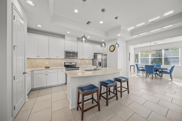 kitchen featuring a center island with sink, white cabinets, a raised ceiling, sink, and stainless steel appliances