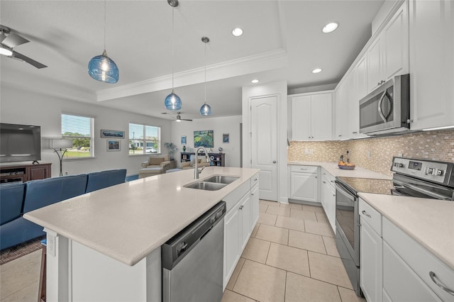 kitchen with sink, stainless steel appliances, pendant lighting, a tray ceiling, and a kitchen island with sink