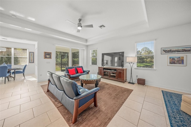 tiled living room with a raised ceiling, ceiling fan, and plenty of natural light