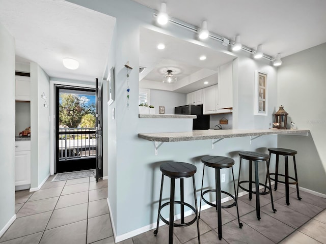 kitchen featuring a kitchen bar, kitchen peninsula, black refrigerator, white cabinets, and light tile patterned flooring