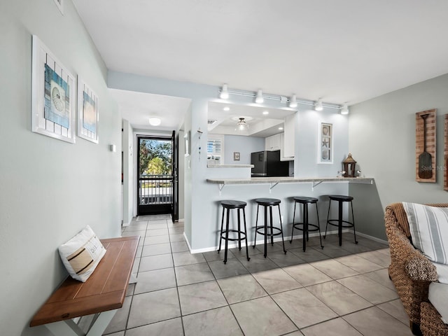 kitchen with a kitchen bar, kitchen peninsula, black fridge, light tile patterned floors, and white cabinets