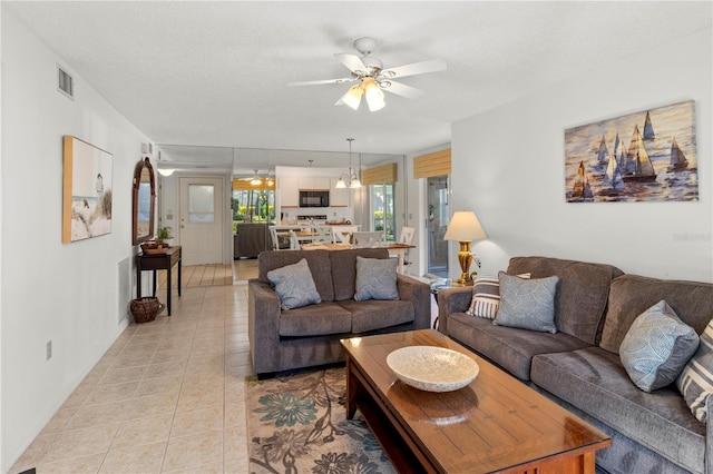 living room with a textured ceiling, light tile patterned floors, and ceiling fan with notable chandelier