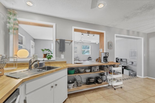 kitchen featuring white cabinetry, sink, stainless steel dishwasher, a textured ceiling, and light tile patterned floors