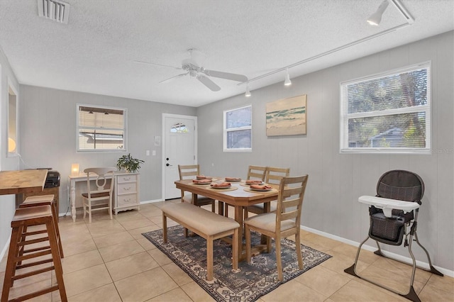 tiled dining room featuring ceiling fan, a textured ceiling, wooden walls, and track lighting