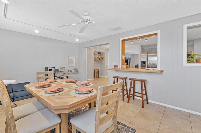 tiled dining room with a textured ceiling, track lighting, ceiling fan, and wooden walls