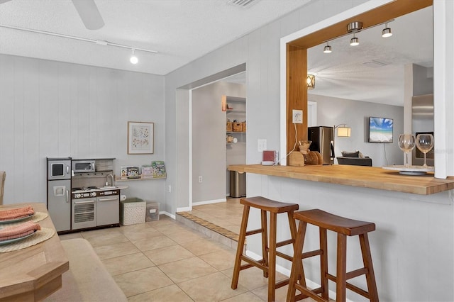 kitchen featuring wooden counters, wood walls, a textured ceiling, a kitchen bar, and light tile patterned floors