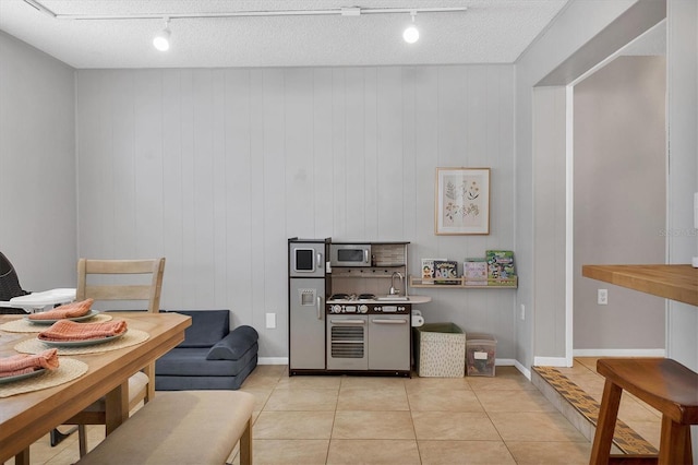 kitchen featuring light tile patterned floors, a textured ceiling, wooden walls, and track lighting