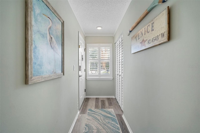 hallway with light hardwood / wood-style floors, crown molding, and a textured ceiling