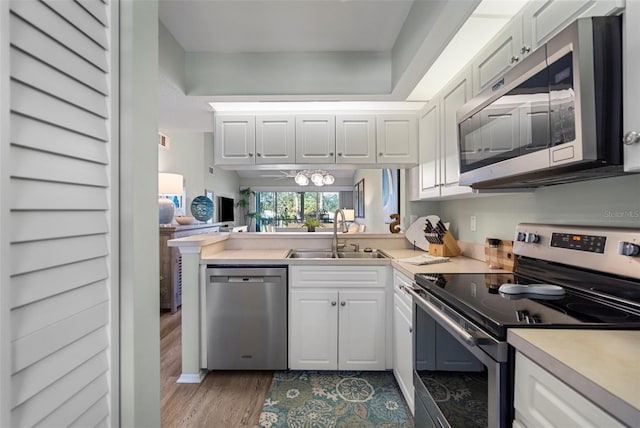 kitchen with kitchen peninsula, light wood-type flooring, stainless steel appliances, sink, and white cabinets