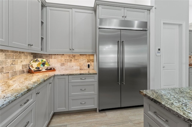 kitchen featuring stainless steel built in refrigerator, gray cabinets, light stone counters, and tasteful backsplash