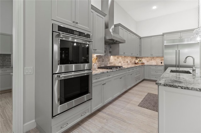 kitchen featuring gray cabinetry, sink, wall chimney exhaust hood, decorative light fixtures, and stainless steel appliances