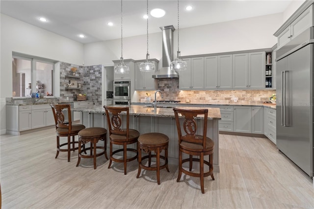 kitchen featuring light stone countertops, stainless steel appliances, a high ceiling, tasteful backsplash, and a center island with sink