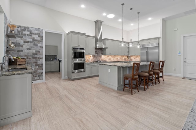 kitchen with gray cabinetry, dark stone counters, sink, wall chimney exhaust hood, and stainless steel appliances