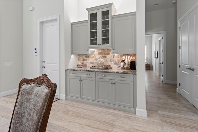 kitchen with backsplash, gray cabinetry, and light stone countertops