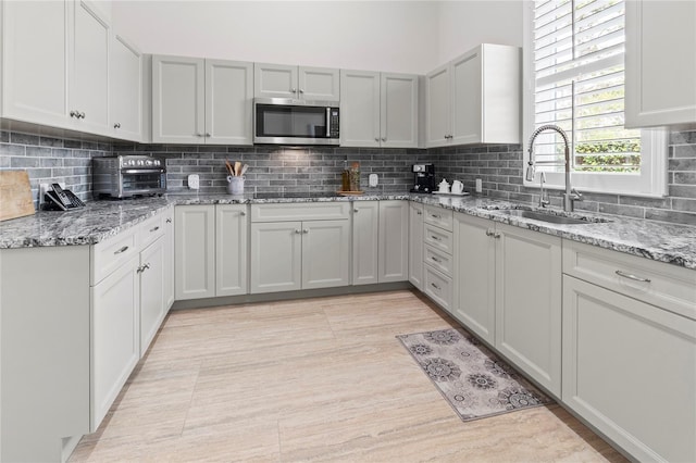 kitchen featuring decorative backsplash, light stone counters, black electric cooktop, sink, and light tile patterned floors