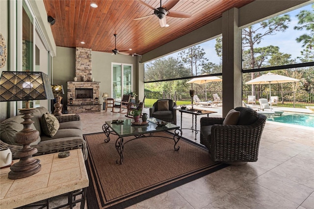 living room with ceiling fan, a stone fireplace, and wood ceiling