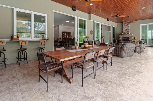 dining space featuring a fireplace, ceiling fan, and wooden ceiling