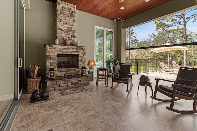 sunroom / solarium featuring a stone fireplace and wood ceiling