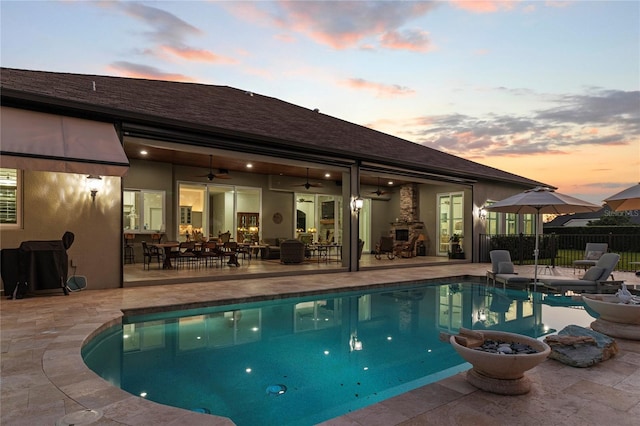 pool at dusk featuring ceiling fan, a patio area, and a fireplace