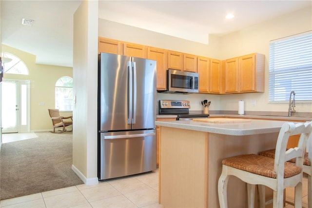 kitchen with sink, light brown cabinets, light colored carpet, a breakfast bar, and appliances with stainless steel finishes