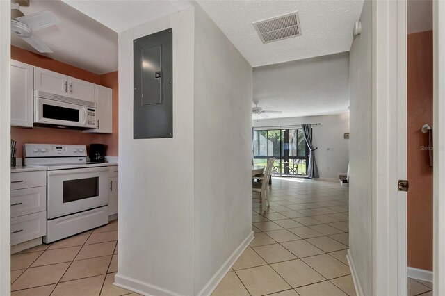 kitchen with white appliances, electric panel, ceiling fan, light tile patterned flooring, and white cabinetry