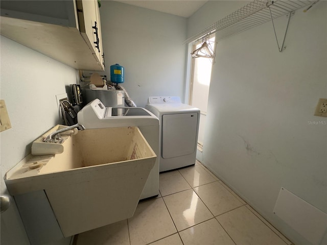 clothes washing area featuring water heater, sink, cabinets, light tile patterned floors, and independent washer and dryer