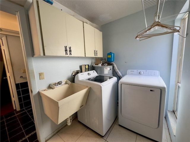 clothes washing area with sink, light tile patterned floors, washer and clothes dryer, cabinets, and a textured ceiling