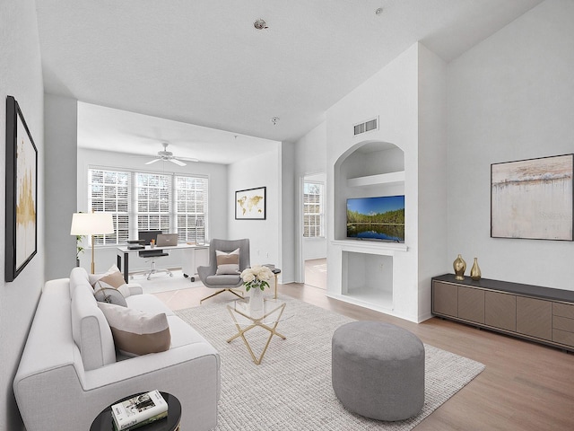 living room featuring ceiling fan, built in features, light hardwood / wood-style floors, and vaulted ceiling