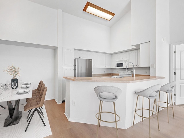 kitchen featuring kitchen peninsula, a kitchen bar, a towering ceiling, white appliances, and white cabinets