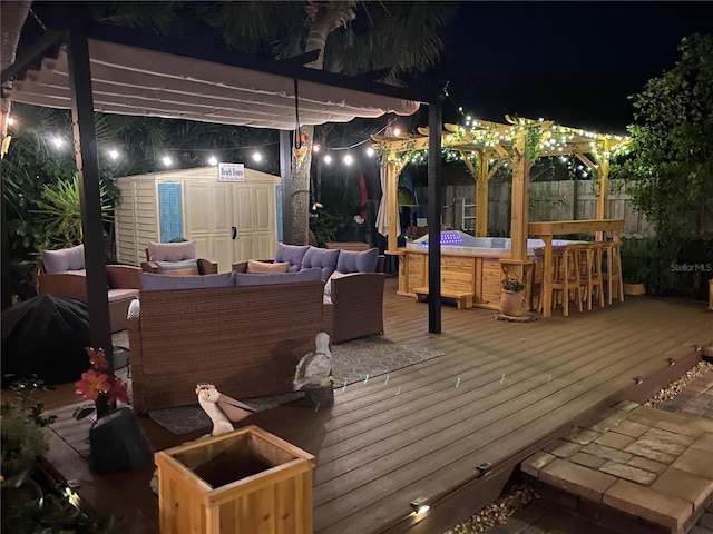 deck at night with a shed, a pergola, an outdoor hangout area, and a jacuzzi