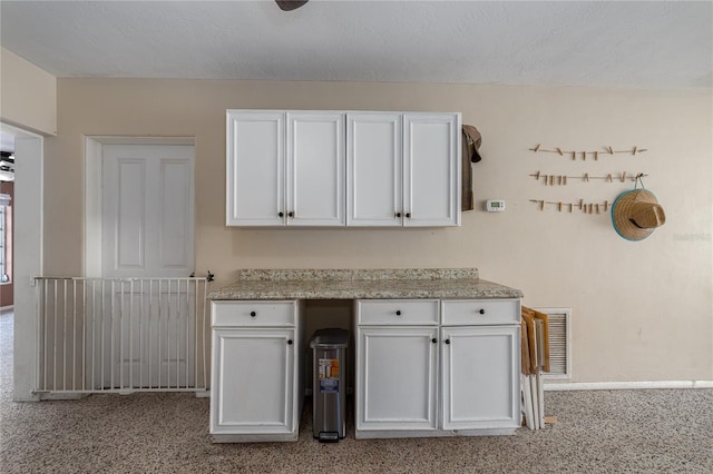 kitchen featuring white cabinets, light stone countertops, and a textured ceiling