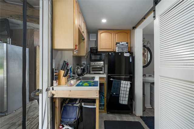 kitchen with a barn door, light brown cabinets, black appliances, and light wood-type flooring