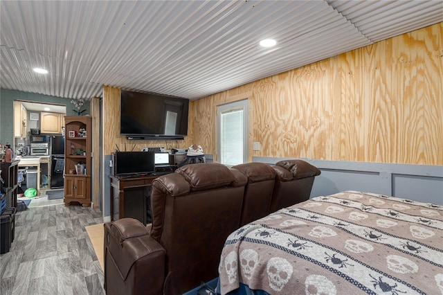 bedroom with wood walls, black refrigerator, and light hardwood / wood-style floors