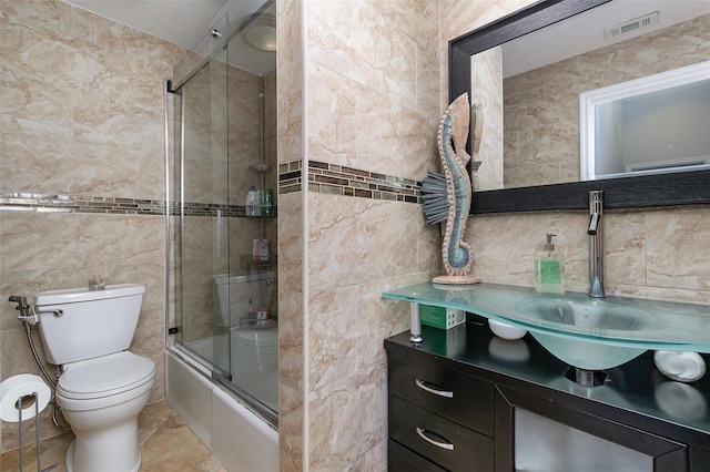 full bathroom with shower / bath combination with glass door, vanity, toilet, and tile walls