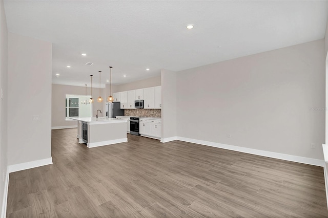 kitchen featuring decorative light fixtures, white cabinetry, tasteful backsplash, an island with sink, and appliances with stainless steel finishes