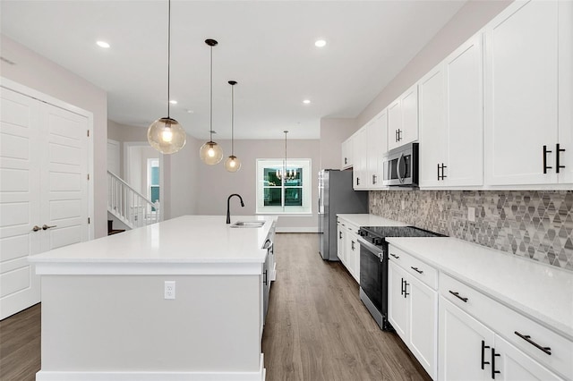 kitchen with appliances with stainless steel finishes, hanging light fixtures, an island with sink, and decorative backsplash