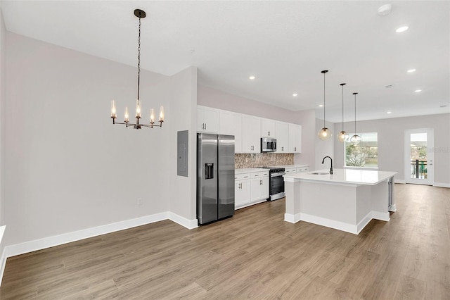 kitchen featuring stainless steel appliances, white cabinets, a kitchen island with sink, and hanging light fixtures