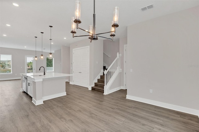 kitchen featuring sink, decorative light fixtures, a center island with sink, and hardwood / wood-style flooring