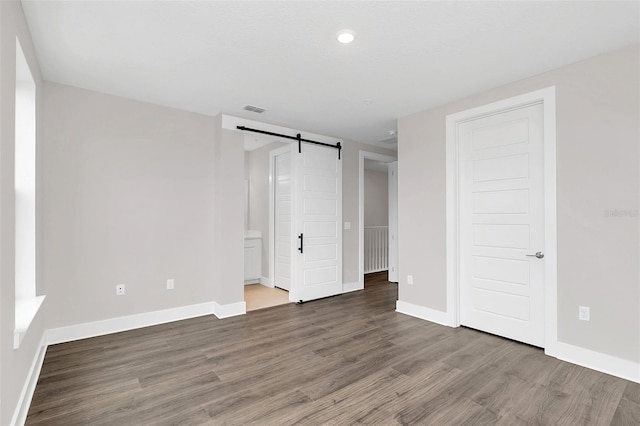 unfurnished bedroom featuring wood-type flooring and a barn door