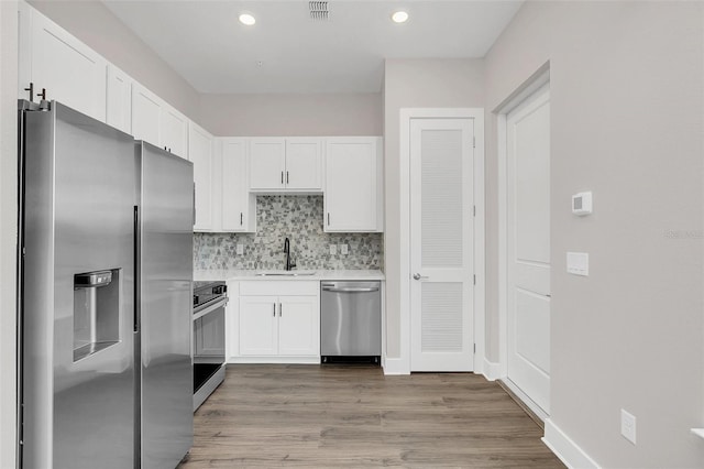 kitchen featuring wood-type flooring, appliances with stainless steel finishes, white cabinets, backsplash, and sink