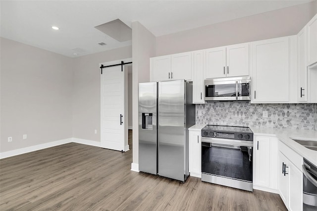 kitchen featuring appliances with stainless steel finishes, a barn door, tasteful backsplash, and white cabinetry