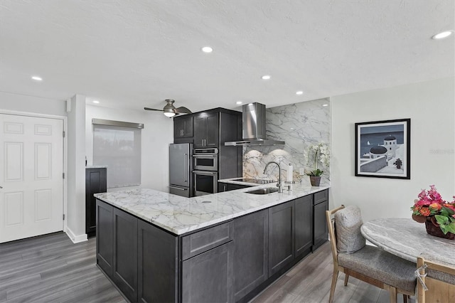 kitchen with a center island, wall chimney exhaust hood, stainless steel appliances, light stone counters, and dark hardwood / wood-style flooring