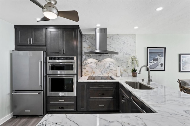 kitchen featuring wall chimney range hood, sink, tasteful backsplash, light stone counters, and stainless steel appliances