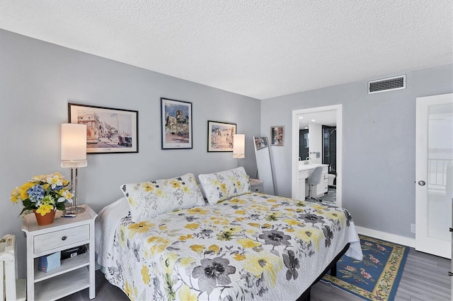 bedroom featuring dark hardwood / wood-style flooring, a textured ceiling, and connected bathroom