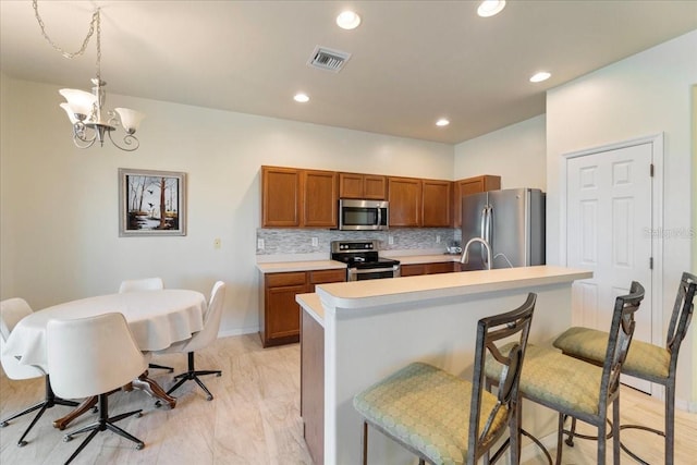 kitchen featuring a breakfast bar area, decorative backsplash, hanging light fixtures, a notable chandelier, and appliances with stainless steel finishes