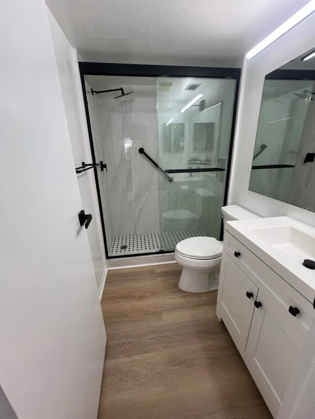 bathroom with hardwood / wood-style floors, vanity, toilet, and a shower with shower door