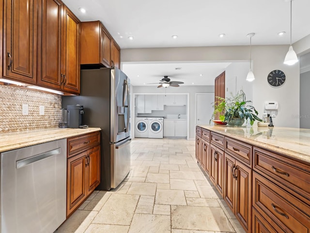 kitchen featuring decorative light fixtures, ceiling fan, washing machine and dryer, appliances with stainless steel finishes, and light stone counters