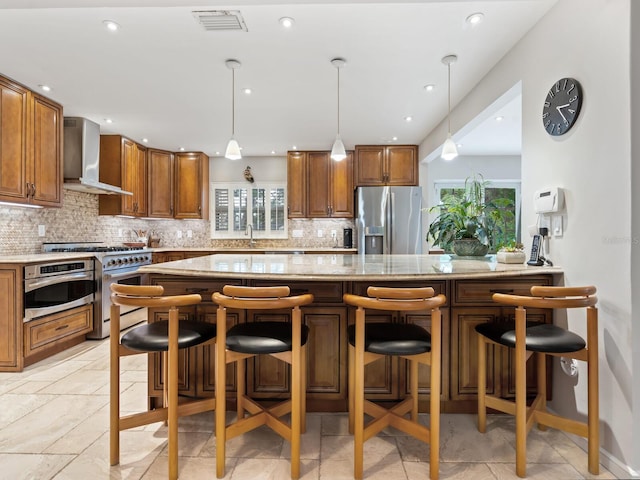 kitchen featuring a kitchen breakfast bar, stainless steel appliances, pendant lighting, and wall chimney range hood