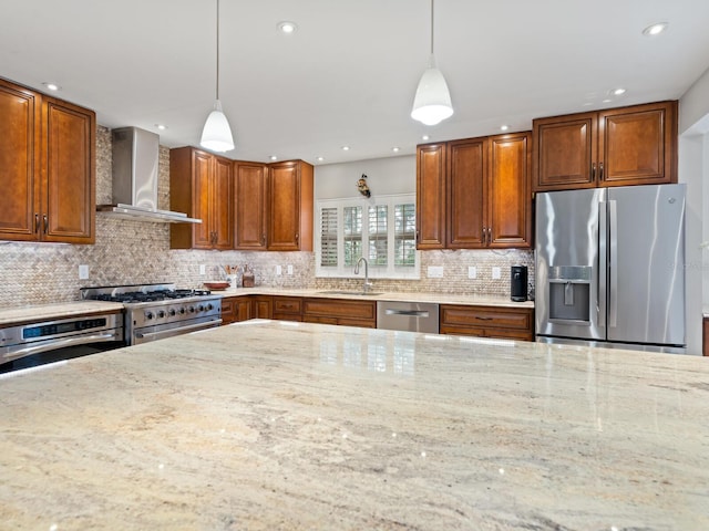 kitchen featuring stainless steel appliances, hanging light fixtures, wall chimney exhaust hood, light stone counters, and sink