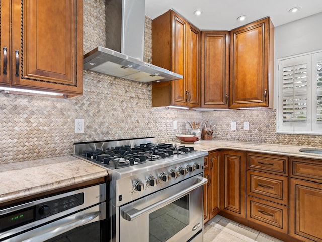 kitchen with decorative backsplash, light stone countertops, wall chimney exhaust hood, and stainless steel appliances